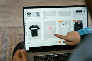 Une personne pointe vers les options de t-shirts dans une boutique en ligne sur l'écran d'un ordinateur portable.