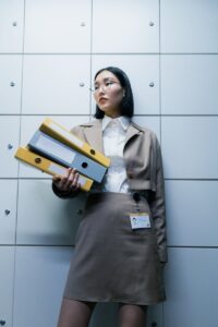 Femme d'affaires en tenue formelle tenant des classeurs dans un environnement de bureau, faisant preuve de professionnalisme.