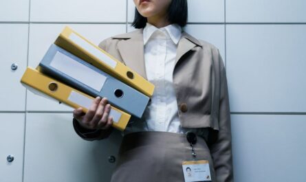 Femme d'affaires en tenue formelle tenant des classeurs dans un environnement de bureau, faisant preuve de professionnalisme.
