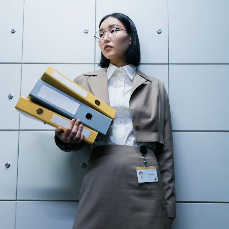 Femme d'affaires en tenue formelle tenant des classeurs dans un environnement de bureau, faisant preuve de professionnalisme.