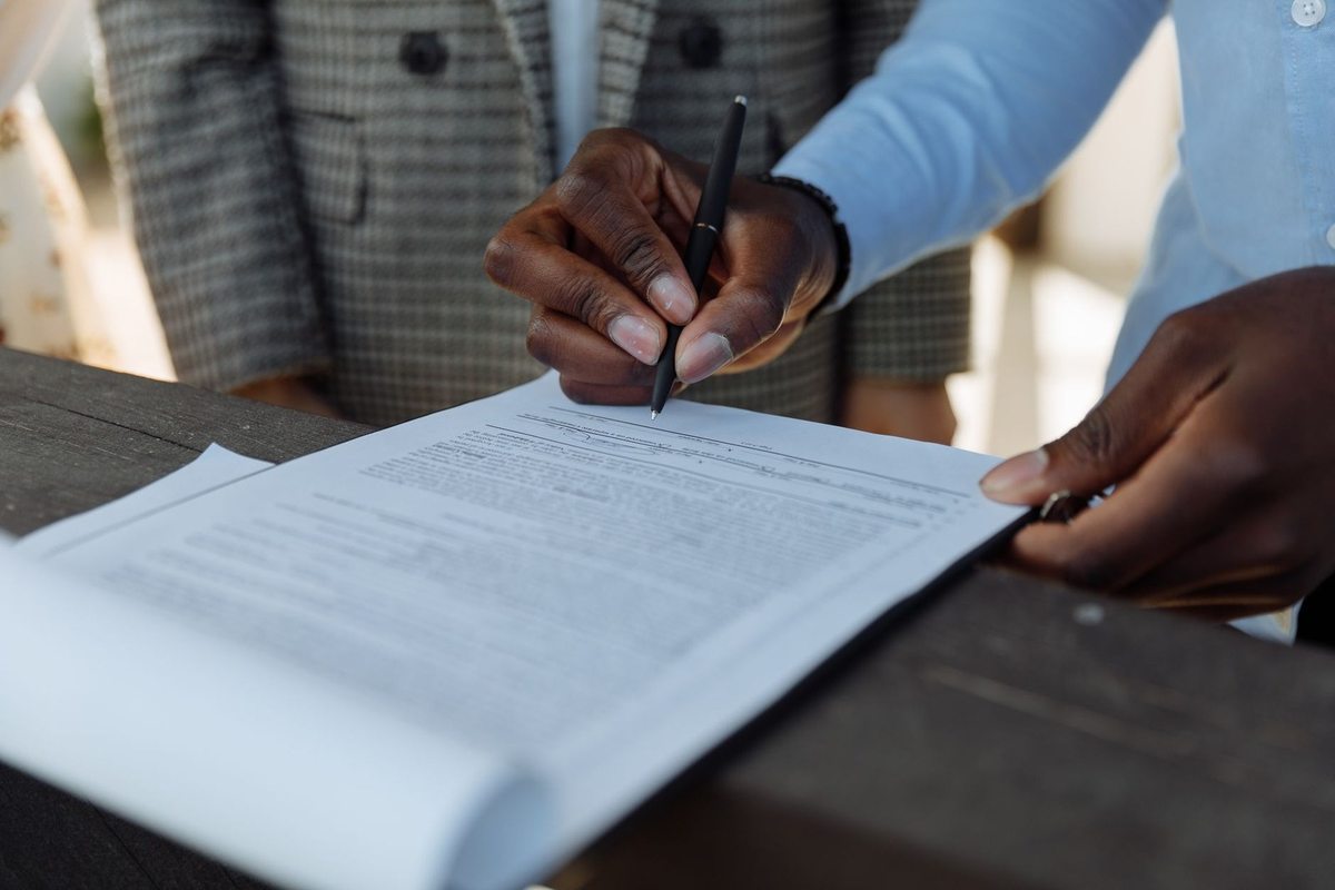 Signature d'un document par une personne noire, un autre individu en costume à proximité