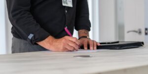 Homme écrivant sur une table avec un stylo, dossier et porte visibles