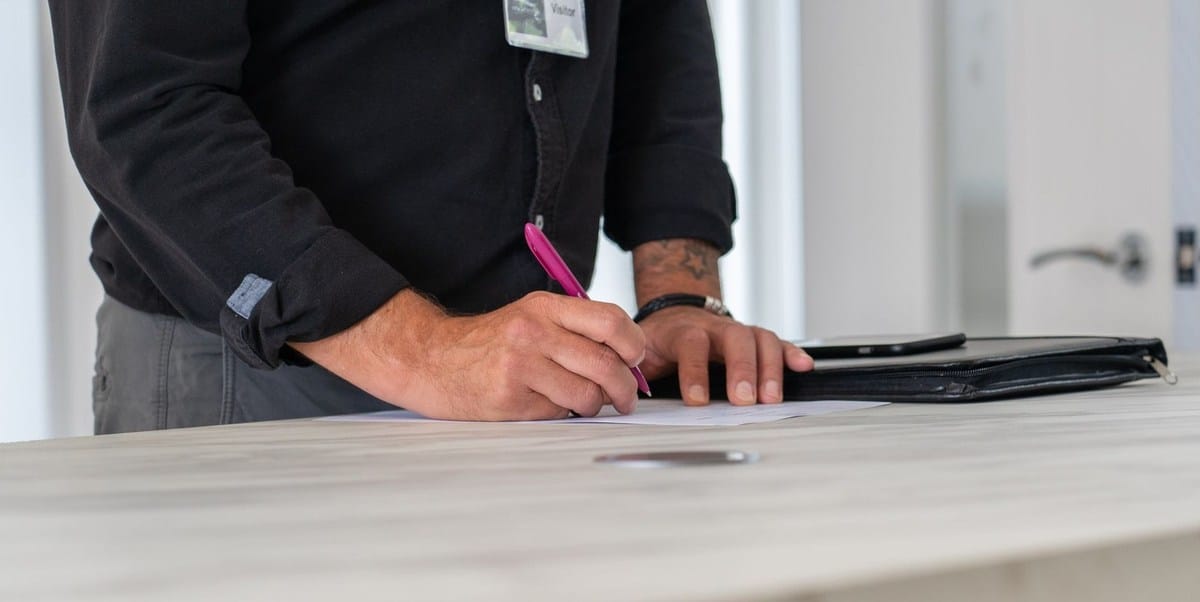Homme écrivant sur une table avec un stylo, dossier et porte visibles
