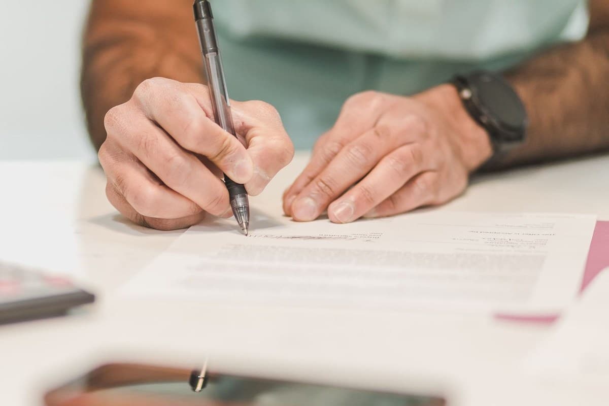 Mains d'une personne écrivant sur un papier avec un stylo noir Mains d'une personne écrivant sur un papier avec un stylo noir