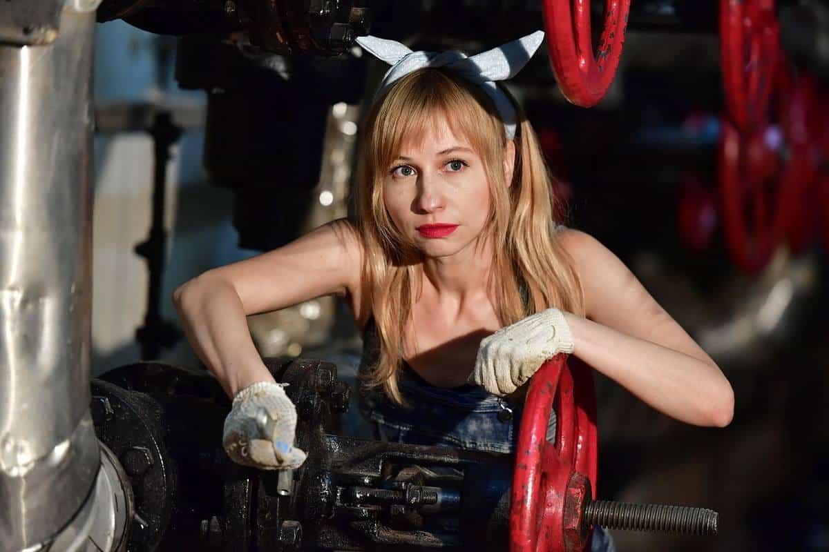 Femme en combinaison usagère manipulant une manivelle rouge dans un environnement industriel