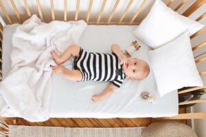 Enfant nu dans une berceuse, couvert d'une plaid, regardant la caméra