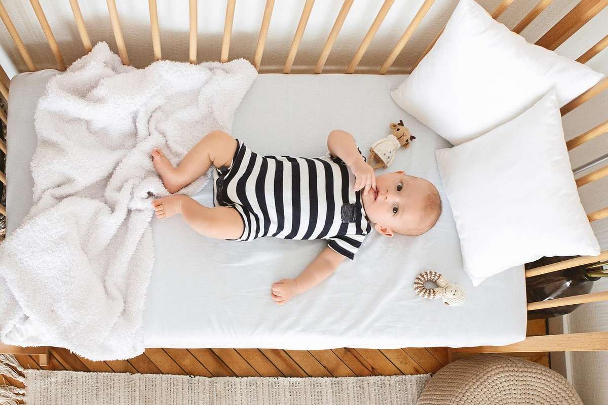 Enfant nu dans une berceuse, couvert d'une plaid, regardant la caméra