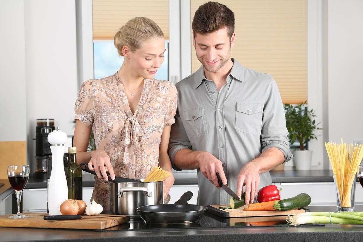 Homme et femme cuisinent ensemble, entourés de légumes et d'ustensiles de cuisine Homme et femme cuisinent ensemble, entourés de légumes et d'ustensiles de cuisine