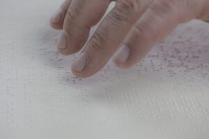 Doigts d'une main parcourant des caractères en braille sur papier blanc