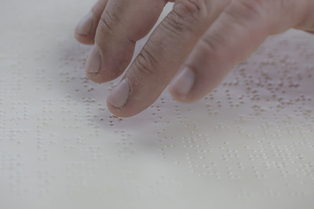 Doigts d'une main parcourant des caractères en braille sur papier blanc
