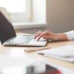 Femme travaillant sur ordinateur portable avec stylo et cahier à côté