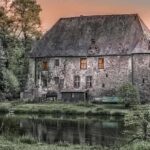 Maison en pierre avec toit d'ardoise au bord d'un étang, entourée d'arbres