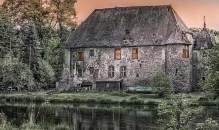 Maison en pierre avec toit d'ardoise au bord d'un étang, entourée d'arbres