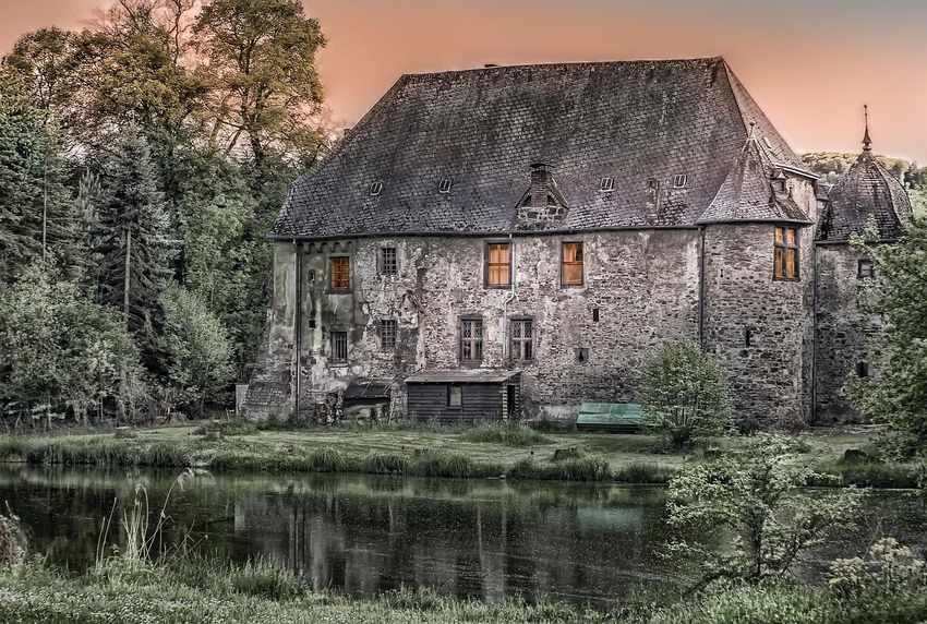 Maison en pierre avec toit d'ardoise au bord d'un étang, entourée d'arbres