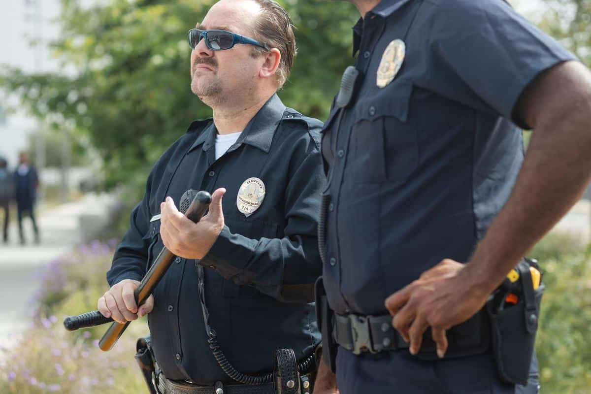 Deux policiers discutent dans un jardin, l'un tient un micro Deux policiers discutent dans un jardin, l'un tient un micro
