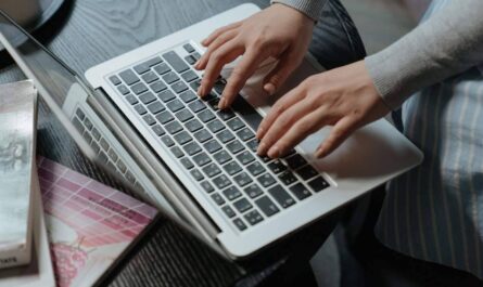 Deux mains tapent sur le clavier d'un ordinateur portable blanc, assis à un bureau