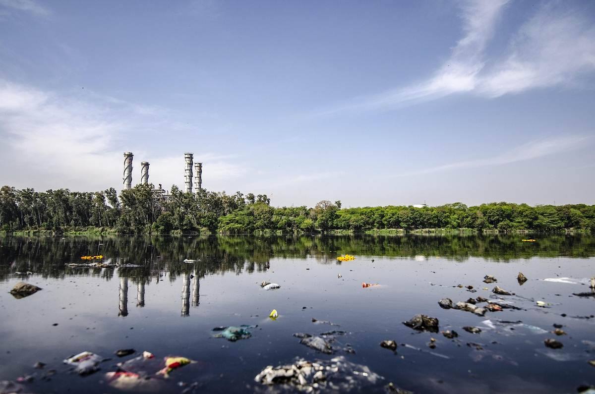 Cheminées industrielles abandonnées se reflètent dans une rivière aux eaux polluées, déchets flottants visibles
