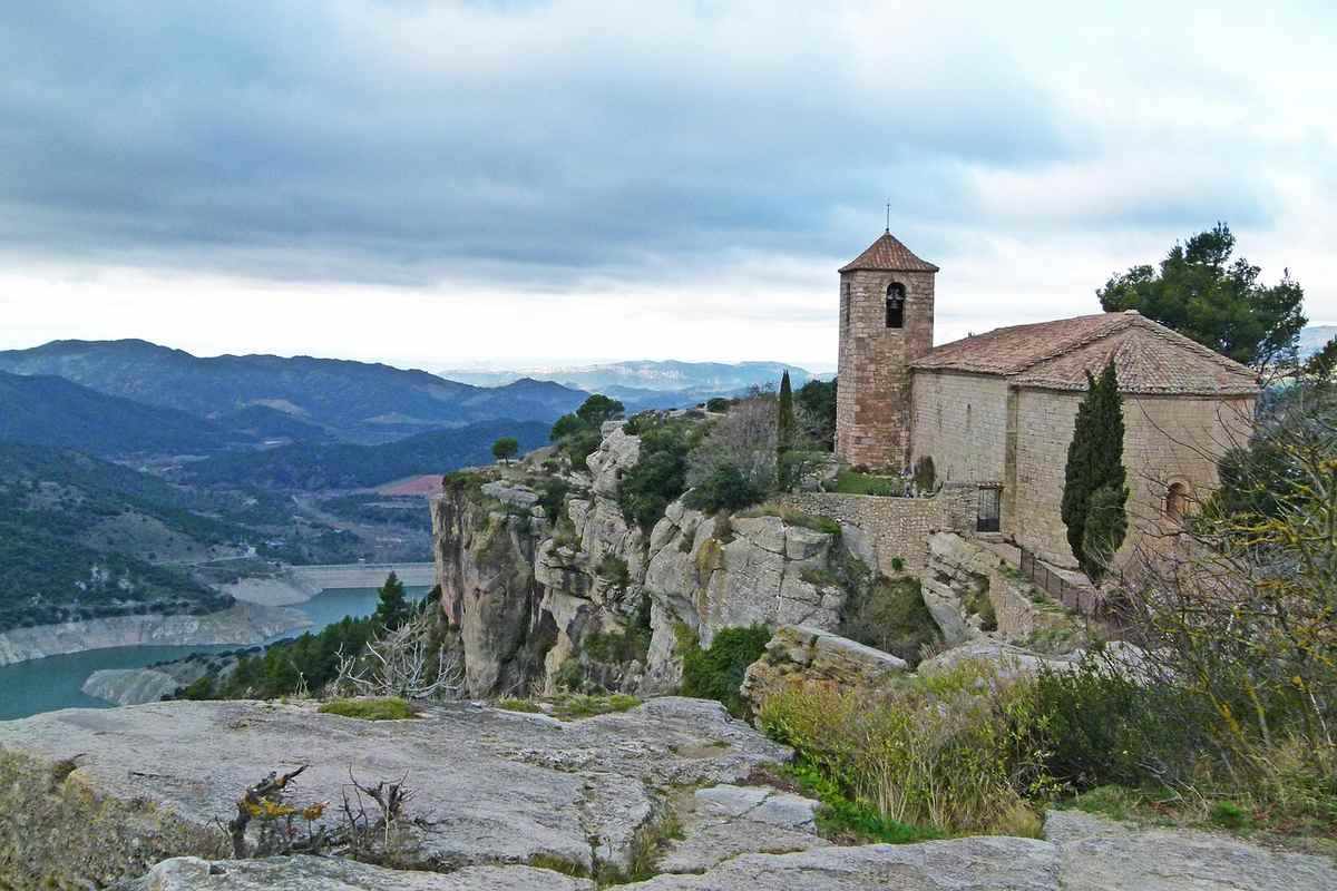 Église perchée sur une falaise avec vue sur une vallée et un ciel nuageux